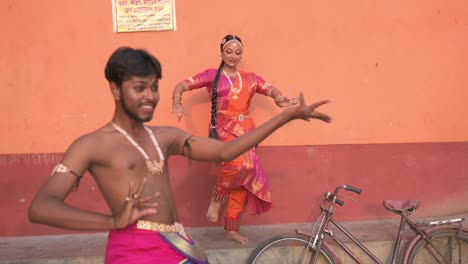Two-Indian-dancers-dancing-Indian-classical-dance-bharatnatyam,-orange-wall-in-background,-slow-motion