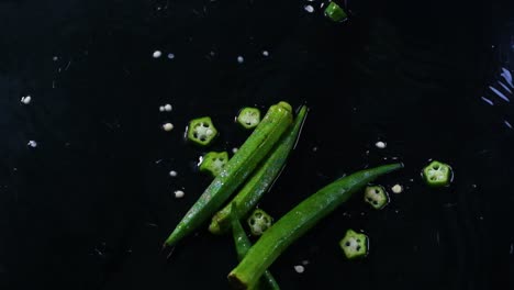 Whole-and-sliced-okra,-or-lady's-fingers,-fall-on-a-wet-surface