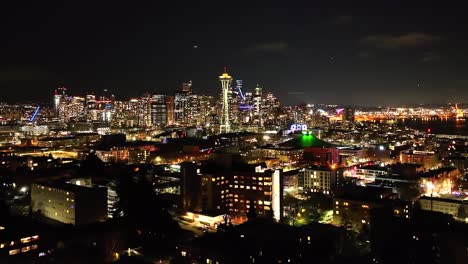 City-of-Seattle-skyline-at-night-from-a-distance,-aerial-over-lit-neighborhood-in-the-dark
