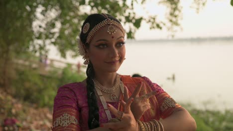 Beautiful-Indian-classical-female-dancer-dancing-bharatnatyam-near-Ganga-river-bank,-slow-motion