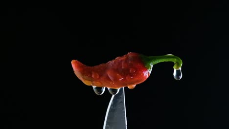 A-red-chili-pepper-on-a-knife-tip,-water-dripping-off