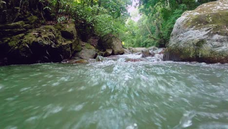 Low-angle-shot-of-rapid-flowing-water-stream-in-rainforest,-splashing-into-camera-lens---slow-motion