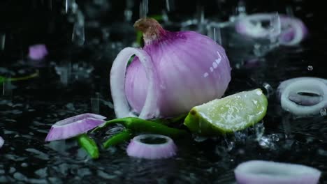 A-red-onion-with-slice,-green-chili-and-lemon-in-a-spray-or-water-on-a-wet-surface