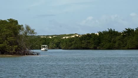 Left-trucking-shot-of-a-small-tour-motor-boat-docked-in-between-tropical-mangroves-on-the-Guaraíras-lagoon-with-sand-dunes-behind-in-Tibau-do-Sul-in-Rio-Grande-do-Norte,-Brazil-on-a-warm-summer-day