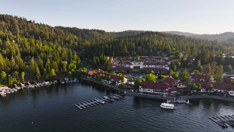 lake-arrowhead-village-at-sunset-with-sun-rays-beaming-onto-the-trees-in-the-hill-tops-over-the-marina-with-boats-in-view-AERIAL-TRUCKING-PAN