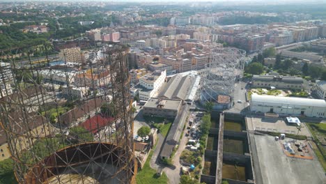 Aerial-drone-forward-moving-shot-flying-high-over-old-iron-structure,-Gazometro-with-the-view-of-Ostiense-district,-Rome-in-Italy-on-a-sunny-day