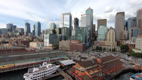 Faszinierender-Drohnenflug-über-Seattles-Geschäftiges-Hafenviertel,-Der-Die-Lebendige-Mischung-Aus-Geschäftsaktivitäten,-Piers-Am-Wasser,-Hoch-Aufragenden-Wolkenkratzern-Und-Architektonischen-Wunderwerken-Zeigt