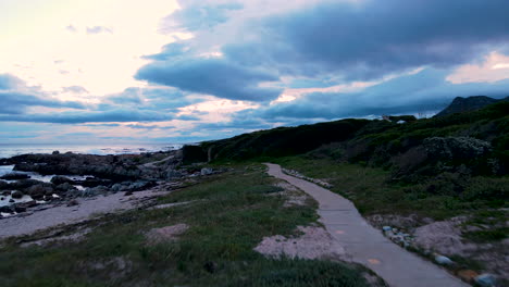 Aerial-dolly-riser-over-coastal-footpath-along-coastline,-sunset-cloudscape
