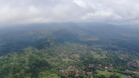 Clouds-above-mountains-and-small-town-bellow-in-Indonesia,-aerial-drone-view