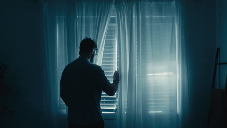Silhouette-of-man-peering-looking-through-blinds-outside,-moody-blue-vibe