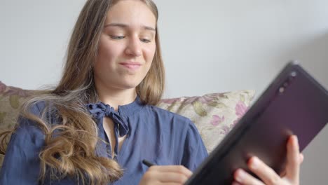 Cute-blue-eyed-teenage-girl-smiling-while-using-tablet-on-the-sofa