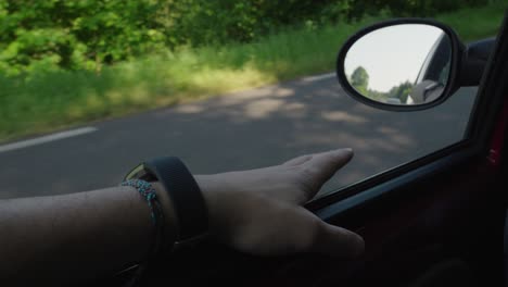 Hand-of-Car-Driver-Resting-next-to-the-Rear-View-Mirror,-Clear-Road-Summer-Day