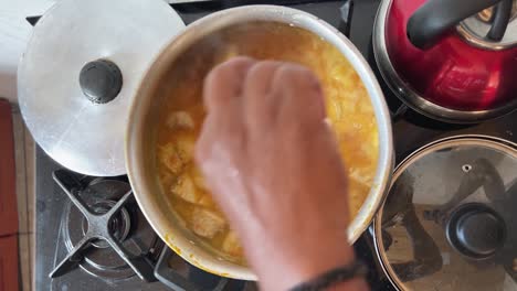 Hand-stirring-a-large-metal-pot-of-delicious-tropical-Brazilian-fish-stew-with-a-wooden-spatula-on-a-gas-stove-in-the-state-of-Rio-Grande-do-Norte-in-Northeastern-Brazil