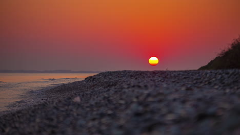 Zeitraffer-Der-Sonne-In-Einem-Roten-Himmel,-Der-Sich-Unter-Dem-Sand-Eines-Strandes-Versteckt