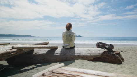 Female-Backpacker-on-Washed-Up-Driftwood-Enjoys-Beautiful-Ocean-View