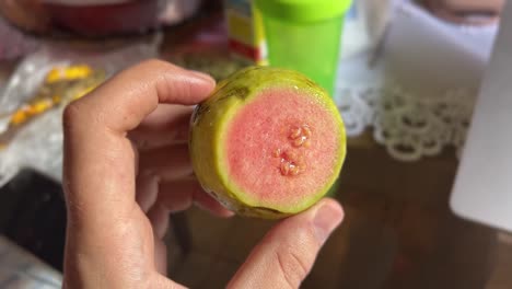 Hand-holding-a-small-cut-up-tropical-guava-fruit-showing-the-pink-with-seeds-inside-and-green-outside-in-the-state-of-Rio-Grande-do-Norte-in-Northeastern-Brazil-on-a-warm-sunny-summer-day