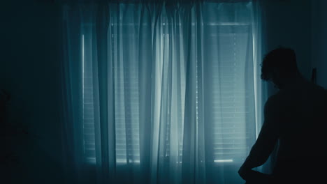 Silhouette-of-muscular-man-curly-hair-putting-shirt-on-in-front-of-window-curtains
