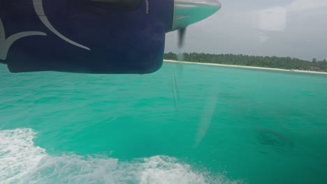 Window-view-of-seaplane-landing-in-tropical-azure-water-with-engine-propeller