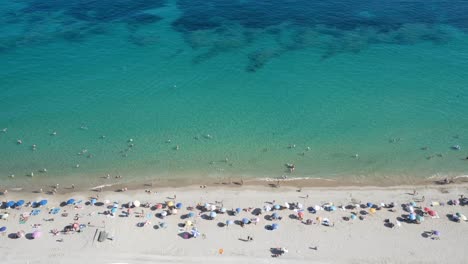 Vista-Panorámica-De-La-Concurrida-Playa-Mediterránea-De-Verano-Con-Arrecife-Visible-4k