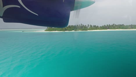 Window-view-of-seaplane-engine-getting-lower-to-water-for-landing,-Maldives