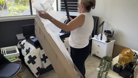 A-mature-woman-unwrapping-flat-pack-furniture-from-a-box-in-a-kid's-bedroom