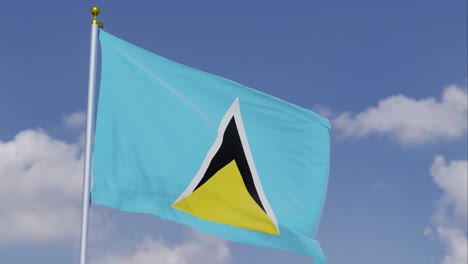 Flagge-Von-St.-Lucia-Bewegt-Sich-Im-Wind-Mit-Einem-Klaren-Blauen-Himmel-Im-Hintergrund,-Wolken-Bewegen-Sich-Langsam,-Fahnenmast,-Zeitlupe