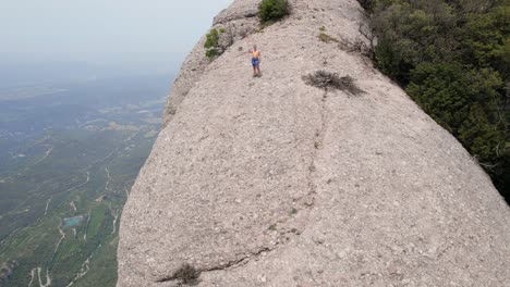 young-woman-saying-goodbye-to-the-camera-in-the-middle-of-the-national-park-of-montserrat-mountain,-drone-moving-away