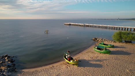 Empty-Fisher-Boats-on-Sandy-Beach-by-the-Gdynia-Orlowo-Pier-Molo,-Poland---Aerial-flyover-at-Sunrise