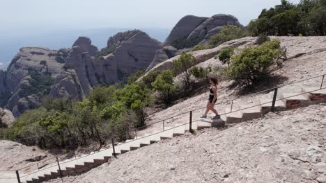 young-woman-walking-in-the-national-park-of-montserrat-mountain,-barcelona,-spain,-drone-shot-following-her,-wellness-and-nature-concept