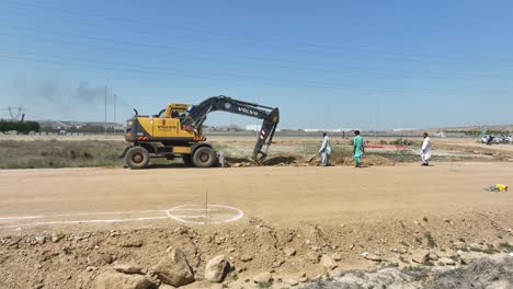 Aerial-Excavator-Digging-Trench-Beside-Gravel-Dirt-Road-In-Pakistan