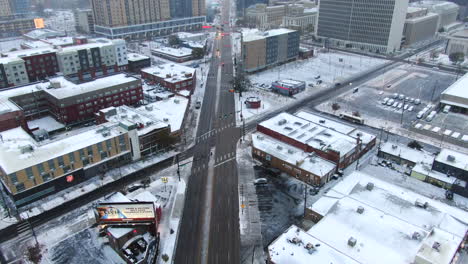 Aerial-cinematic-drone-downtown-Denver-Colorado-city-buildings-Coors-sign-snowing-freezing-cold-winter-day-gray-bird-dramatic-city-car-traffic-cross-intersection-middle-road-pan-down-movement
