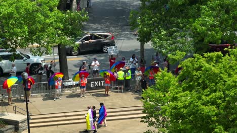 Protesters-with-Christian-religious-banner-demonstrating-at-entrance-or-exit-of-park-area-during-LGBTQ-Pride-Parade-in-USA---Aerial-top-down