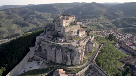 Close-aerial-view-of-The-Medieval-Castle-of-Morella-on-top-of-a-rocky-hill-surrounded-by-green-Mediterranean-pine-trees-in-Spain