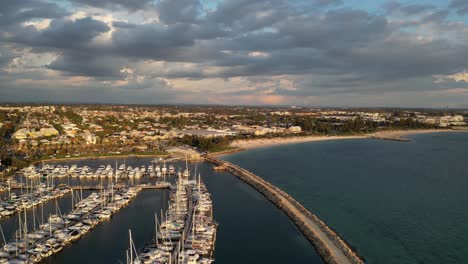 Aerial-establishing-shot-of-Marina-Yacht-during-golden-sunset-and-beautiful-Australian-coastline-in-background---Dark-Clouds-at-sky-in-Western-Australia---Drone-flyover