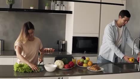 Cheerful-young-family-couple-cutting-fresh-vegetable-salad,-having-fun-cooking-together-im-modern-loft-interior-kitchen,-happy-husband-helping-prepare-healthy-meal---washing-yellow-peper-in-sink