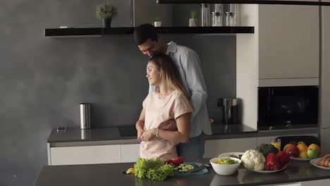 Attractive-young-caucasian-couple-meet-early-morning-in-the-home-modern-kitchen.-Standing-in-front-the-counter-embracing-and-then-wife-kissing-her-husband.-Happy-married-couple-enjoying-morning