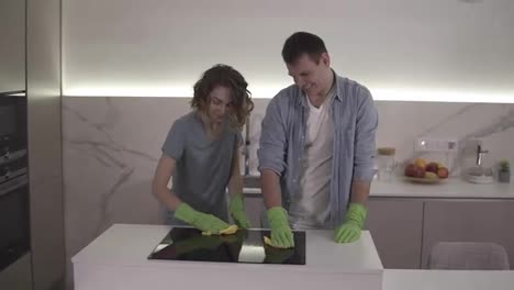 Couple-with-four-hands-cleaning-cooktop-cooking-panel-on-kitchen.-Young-man-and-woman-cleaning-up-the-perfect-surface-of-black-ceramic-kitchen-stove-using-gloves-and-mop.-Having-fun.-Slow-motion