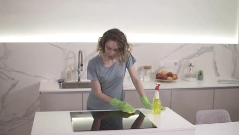 Caucasian-girl-cleaning-cooktop-cooking-panel-on-kitchen.-Young-woman-cleaning-up-the-perfect-surface-of-black-ceramic-kitchen-stove-and-counter-using-gloves-and-mop.-Having-fun-and-singing.-Slow-motion