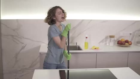 Happy-young-woman-cute-housewife-is-washing-floor-with-mop-and-dancing-and-singing-at-home-in-kitchen-enjoying-housework.-People,-modern-lifestyle-and-youth-concept