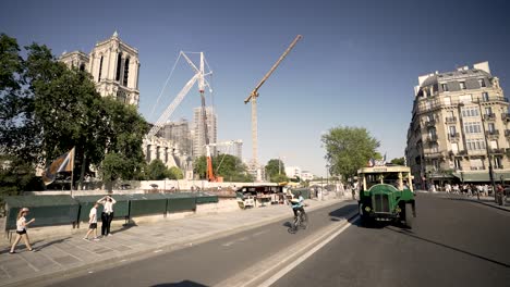 Notre-Damme-Cathedral-with-cranes-being-repaired-from-fire,-book-sellers-in-front-and-vintage-bus-following,-Looking-back-from-vehicle-shot