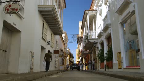 Old-Cartagena,-Colombia-man-walks-between-white-buildings