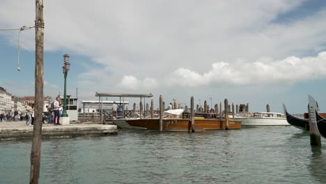 Man-Sieht-Leere-Boote-Sanft-Neben-Dem-Canal-Grande-In-Venedig-Schweben,-Während-Gondeln-Mit-Touristen-Vorbeifahren