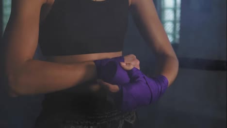 Closeup-view-of-muay-thai-female-boxer-wrapping-bandages-on-her-hands-before-fight-in-dark-room-with-smoke.-Shot-in-4k