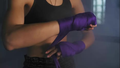 Closeup-view-of-female-hands-being-wrapped-for-boxing-in-dark-room-with-smoke.-Young-fit-woman-wrapping-hands-with-purple-boxing-bandage.-Shot-in-4k