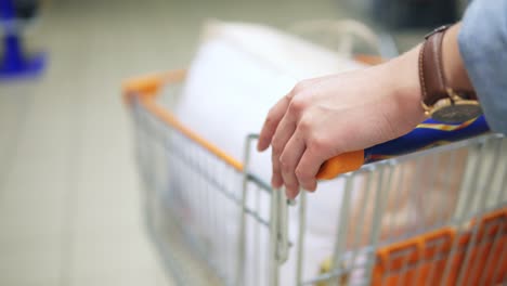 Close-up-of-a-woman's-hands-holding-and-pushing-a-trolley-with-goods-in-the-supermarket.-Backside-view