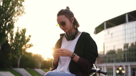 Low-angle-footage-of-a-pensive-girl-sitting-outdoors-on-the-street-or-park-with-her-smartphone-in-hands.-Profile-of-a-thoughtful