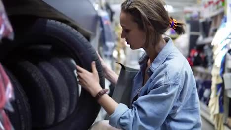 Cute-girl-in-big-shopping-center-selecting-car-tyres.-Examination.-Buyer.-Rows-of-different-car-tyres.-Side-view