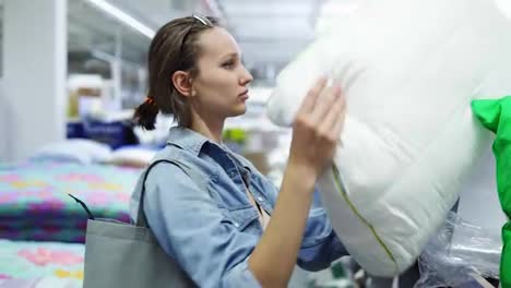 Cute,-positive-caucasian-woman-in-the-store.-Shopping-concept.-Take-a-soft-pillow-from-the-rack-and-lay-her-head-on.-Take-a-nap,-have-fun,-smiling