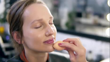 Make-up-artist-gently-put-on-base-foundation-on-a-model's-face-using-a-sponge.-Close-up-of-model's-face