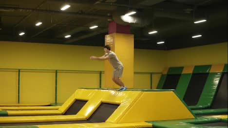 Young-male-athlete-in-beige-t-shirt-and-shorts-jumps-on-trampoline-and-enjoys-doing-front-double-somersaults.-Youth,-sport,-gymnastics.